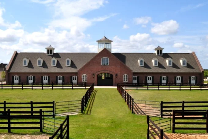 The main brick barn at The Stables at Le Bocage with cupola, dormers, and fenced paddocks
